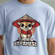 Light blue dog t-shirt with a cartoon chihuahua dog wearing a hat and scarf, and text 'Turning Yapanese' on a plain background.